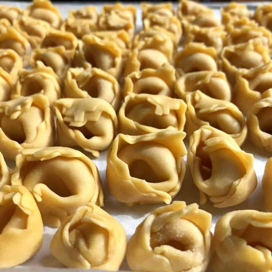 a tray filled with rows of homemade raw tortellini