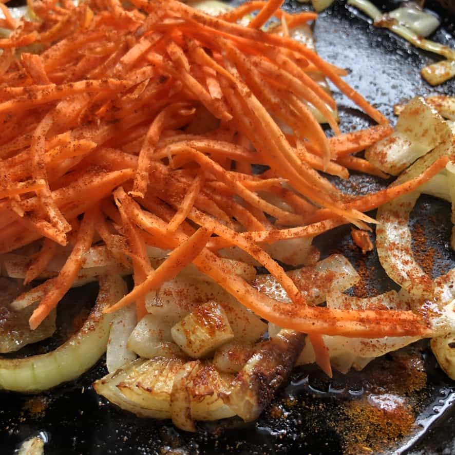 julienned carrots and large sliced onions sautéing in a skillet
