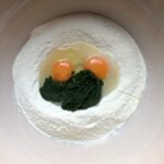 eggs, EVOO, and spinach in the well of a mound of semolina flour
