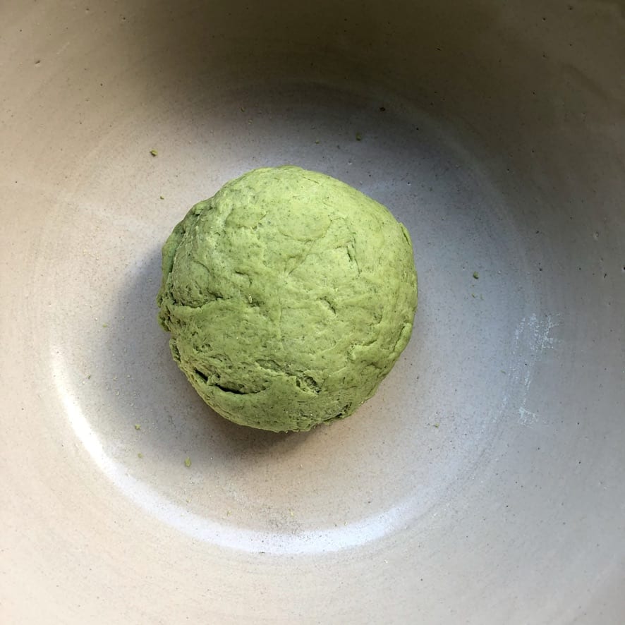 a very shaggy and rough looking green ball of spinach pasta dough after being kneaded for