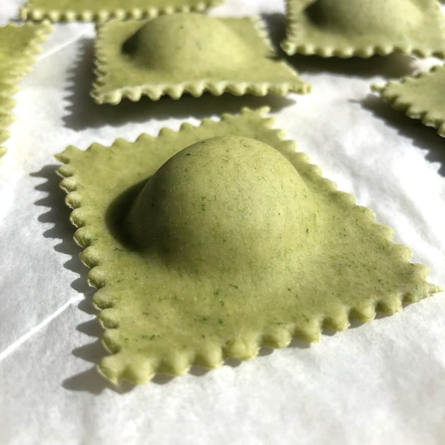 raw green filled ravioli on a parchment-lined sheet pan