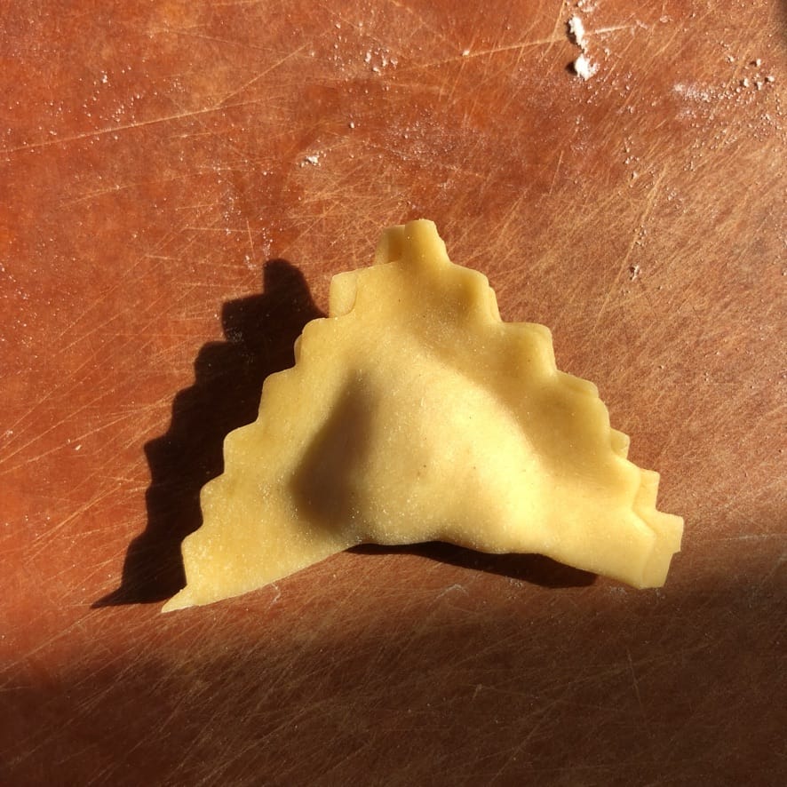 a square of pasta with tortellini filling enclosed inside to create a triangle