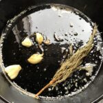 melted butter, crispy rosemary, and smashed toasted garlic in a cast iron skillet ready to separate the solids from the now-seasoned butter