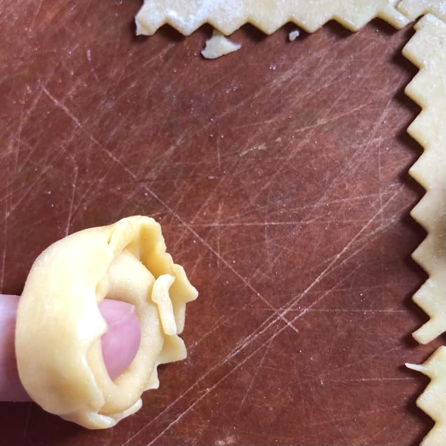 the sealed tortellini with the folded down point now wrapped around a finger and pressed to seal it into a circle resembling a belly button