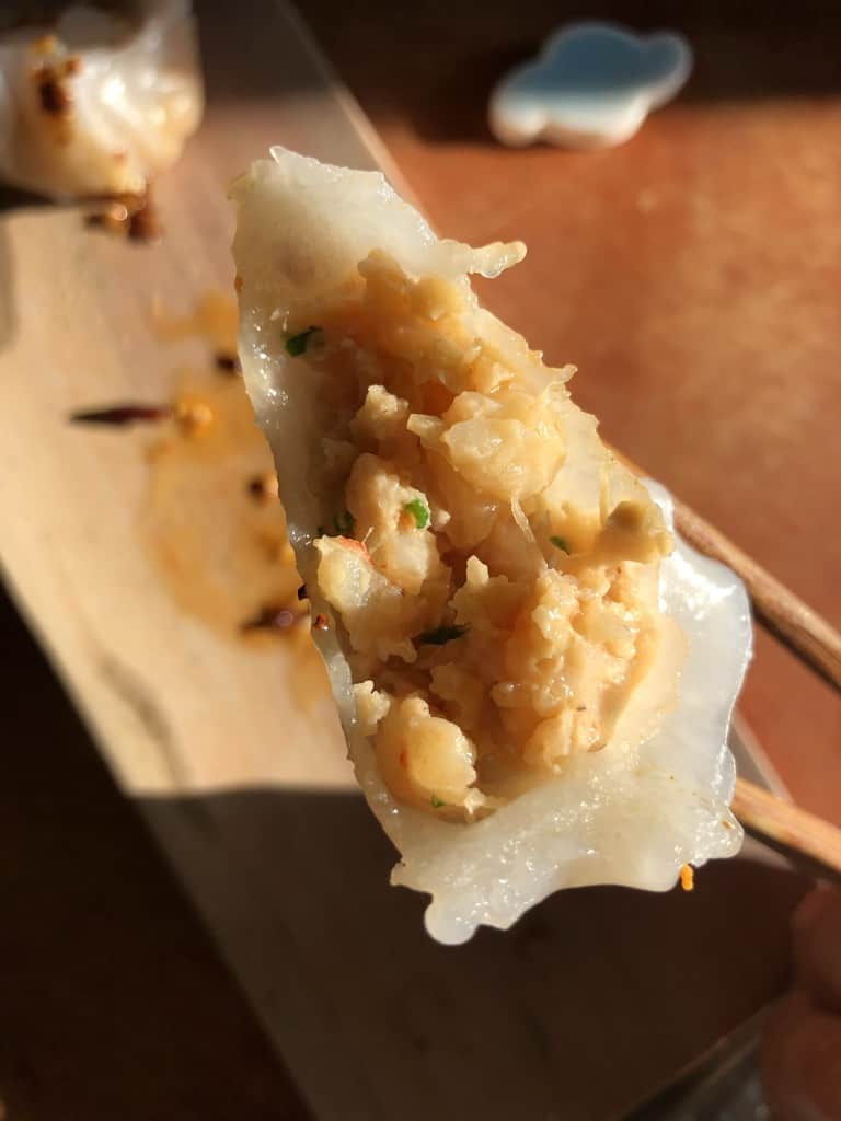 a bit taken out of a crystal dumpling being held by a pair of chopsticks to see the large pices of shrimp inside