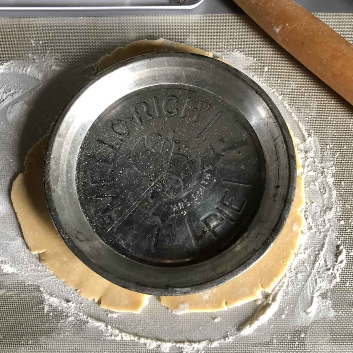 A pie plate set atop a rolled out crostata dough to make sure it's large enough to cover the bottom of the pie plate.