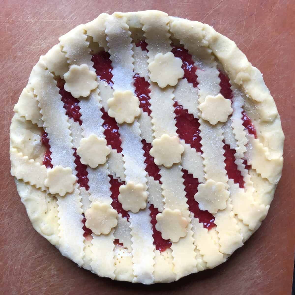 zigzagged edged lattice top covered strawberry jam crostata in a diamond pattern and scalloped circles on top