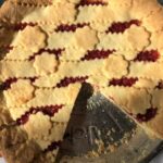 a golden brown lattice-topped strawberry crostata di marmellata with scallop cutouts on top of the lattice and a piece removed from the pie tin