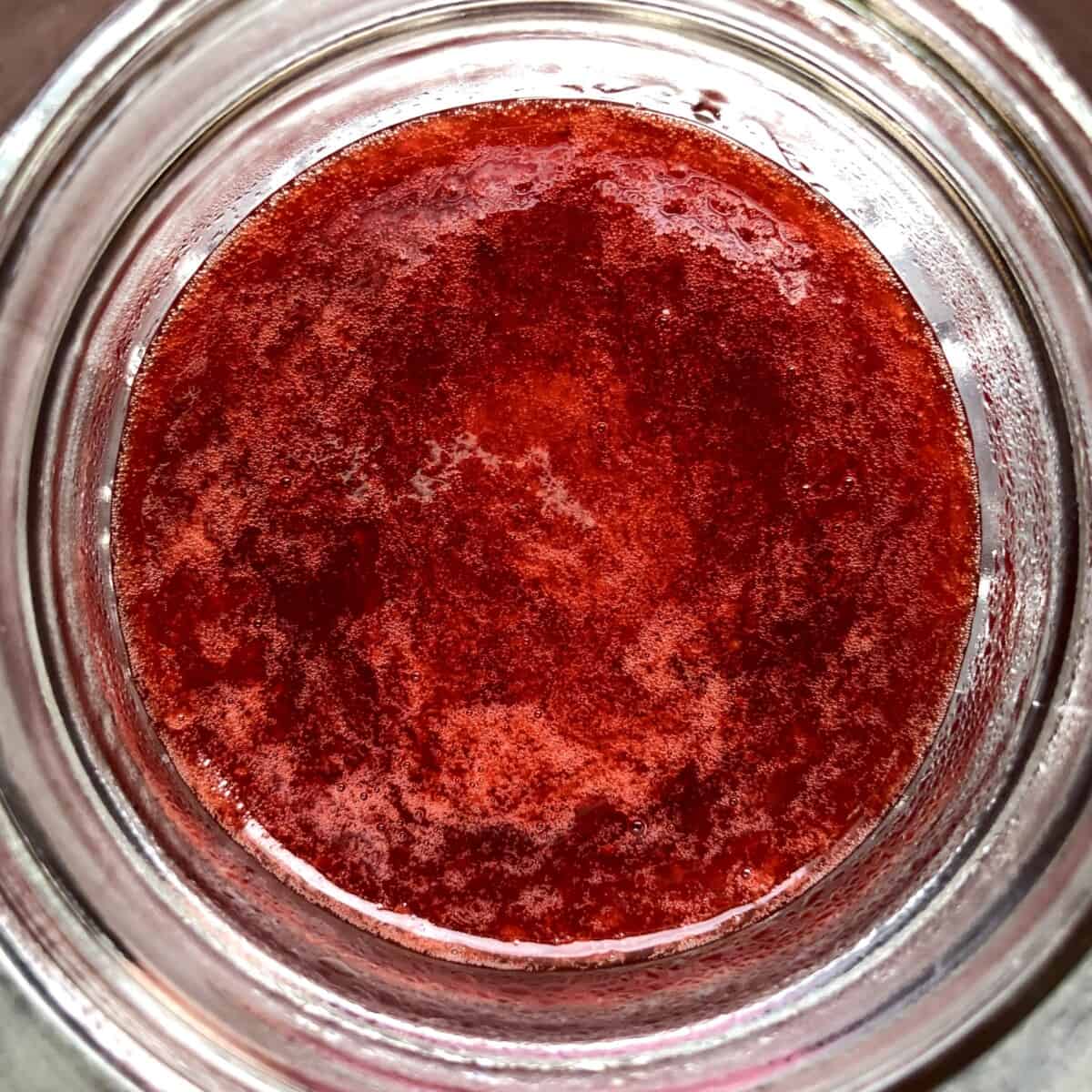 a view down into a widemouth Mason Ball glass canning jar filled with bright deep red homemade strawberry jam