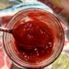a spoon full of homemade strawberry jam being taken out of the widemouth mason Ball jar