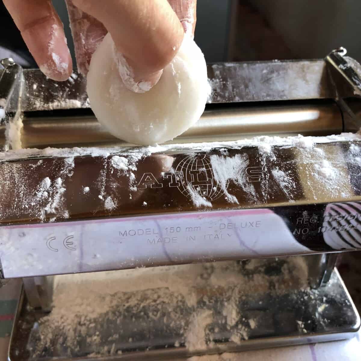 putting a piece of portioned dumpling dough into a pasta machine to roll it