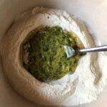eggs, EVOO, and spinach in the well of a mound of semolina flour being mixed with a fork