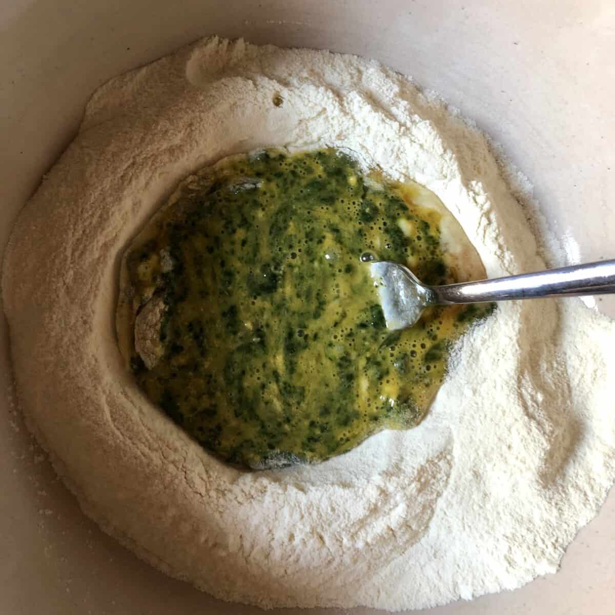 eggs, EVOO, and spinach in the well of a mound of semolina flour being mixed with a fork
