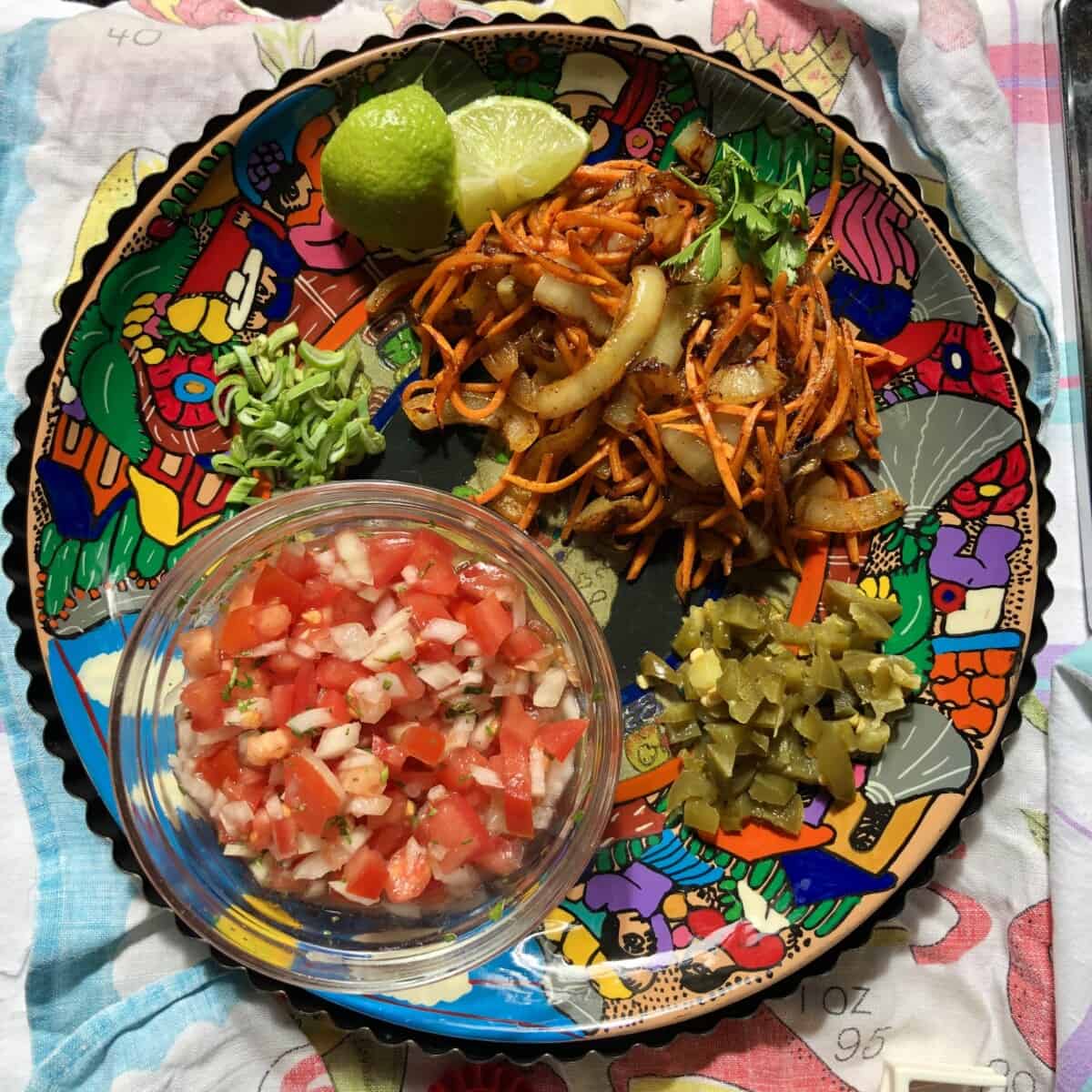 a colorful platter with homemade salsa, 2 wedges of lime, sautéed smoked paprika carrots and caramelized onion mixture, chopped pickled jalapeños, and sliced scallions