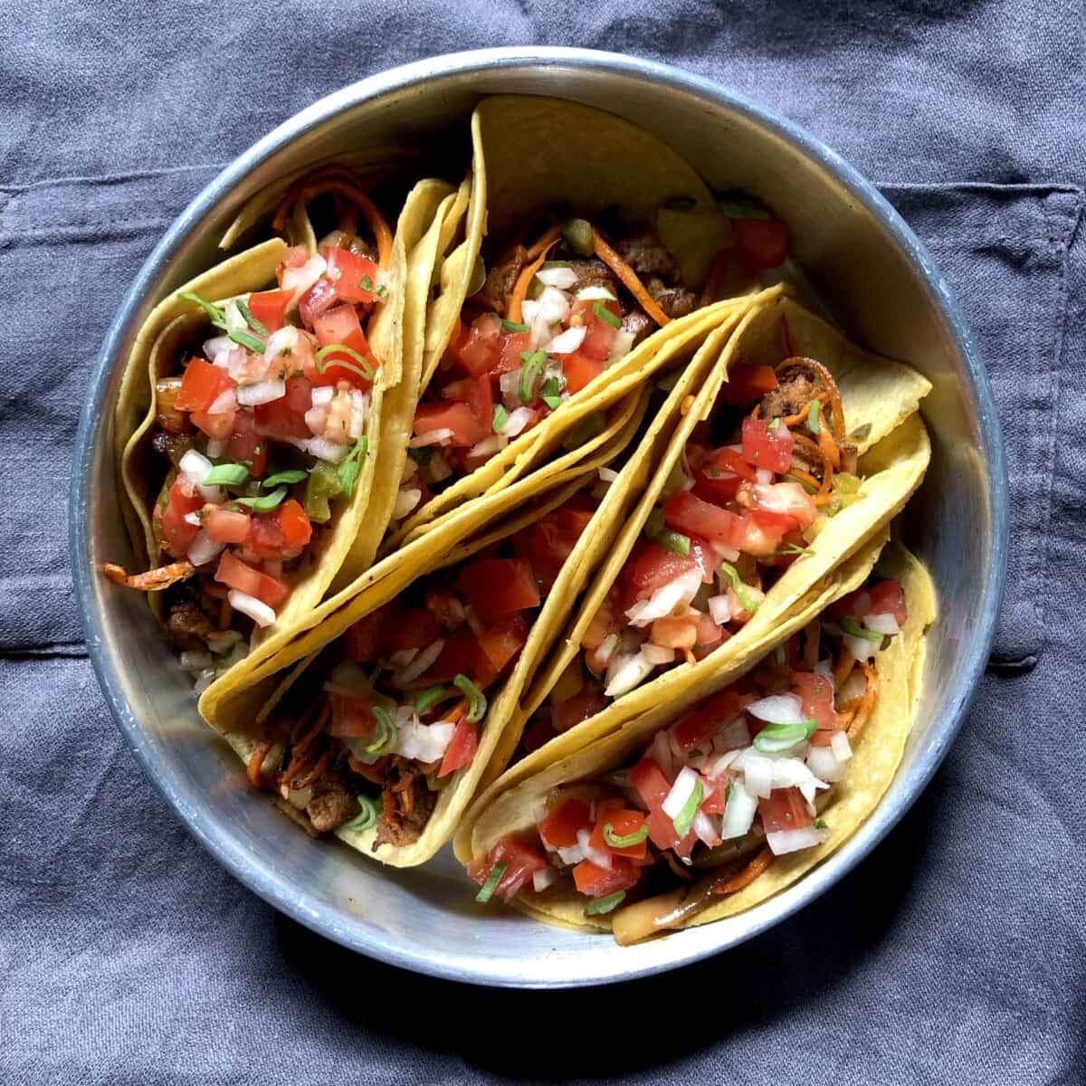 5 corn tortilla steak tacos in a round cake pan held up by each other and topped with salsa, jalapeños, and cilantro