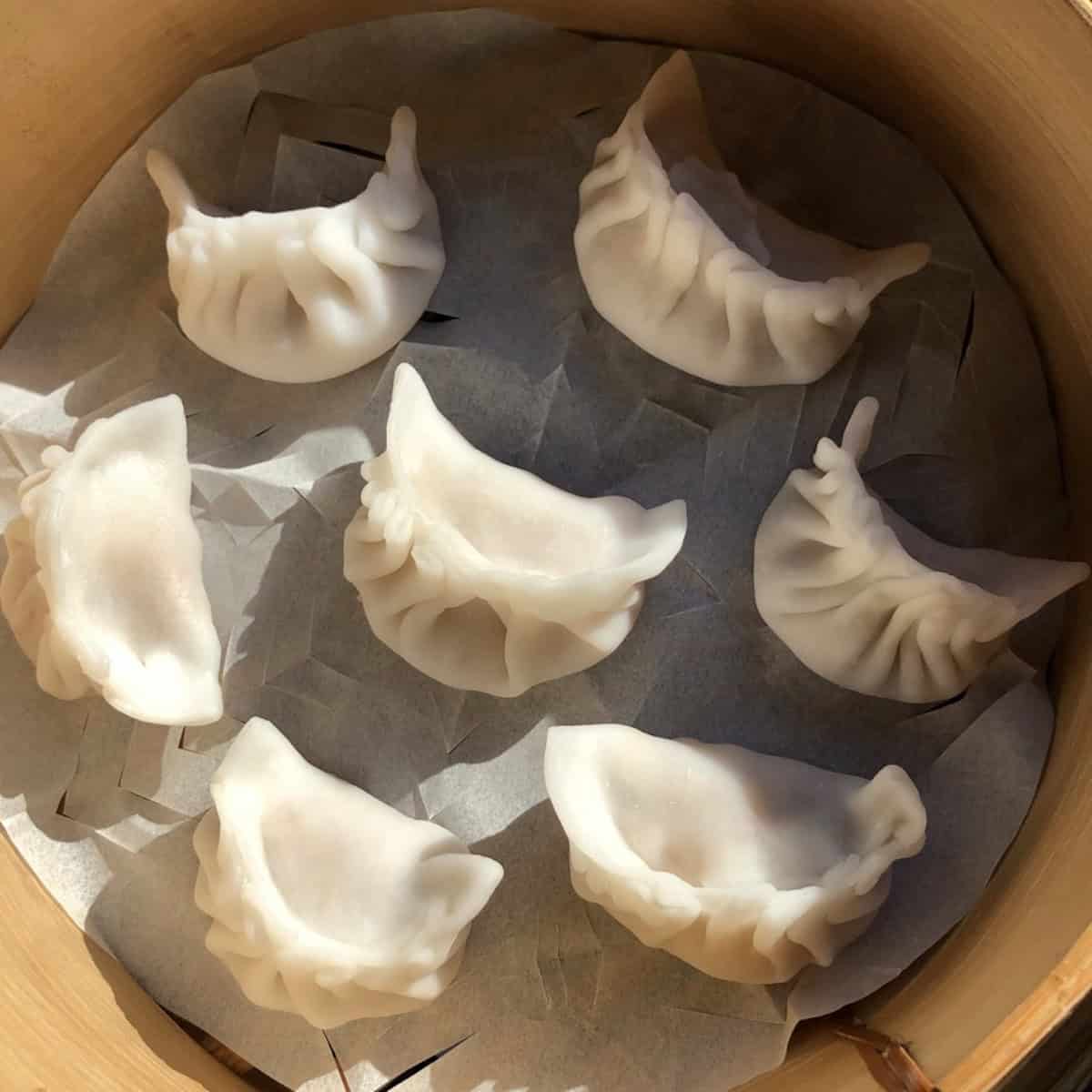 A parchment lined tray of perfectly pleated unsteamed har gow with opaque wrappers ready to steam or freeze.
