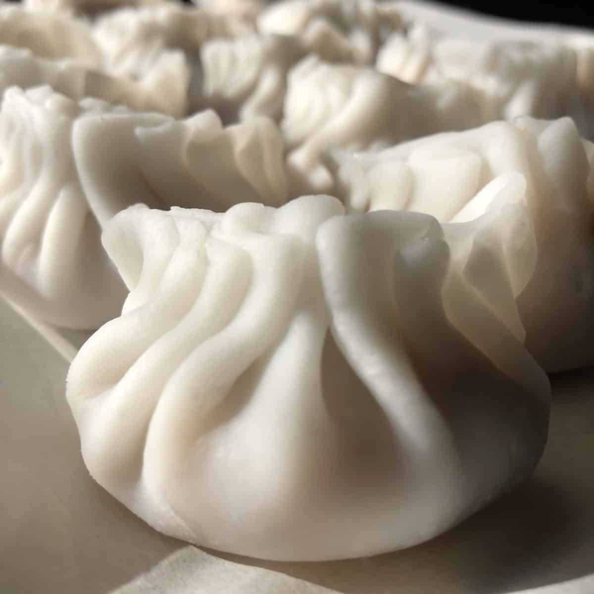 A parchment lined tray of perfectly pleated unsteamed har gow with opaque wrappers ready to steam or freeze.
