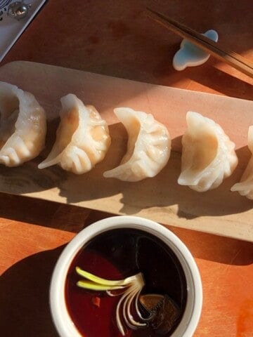 Shrimp dumplings har gow arranged on a tray with dipping sauce garnished with a scallion flower, a classic dim sum recipe.
