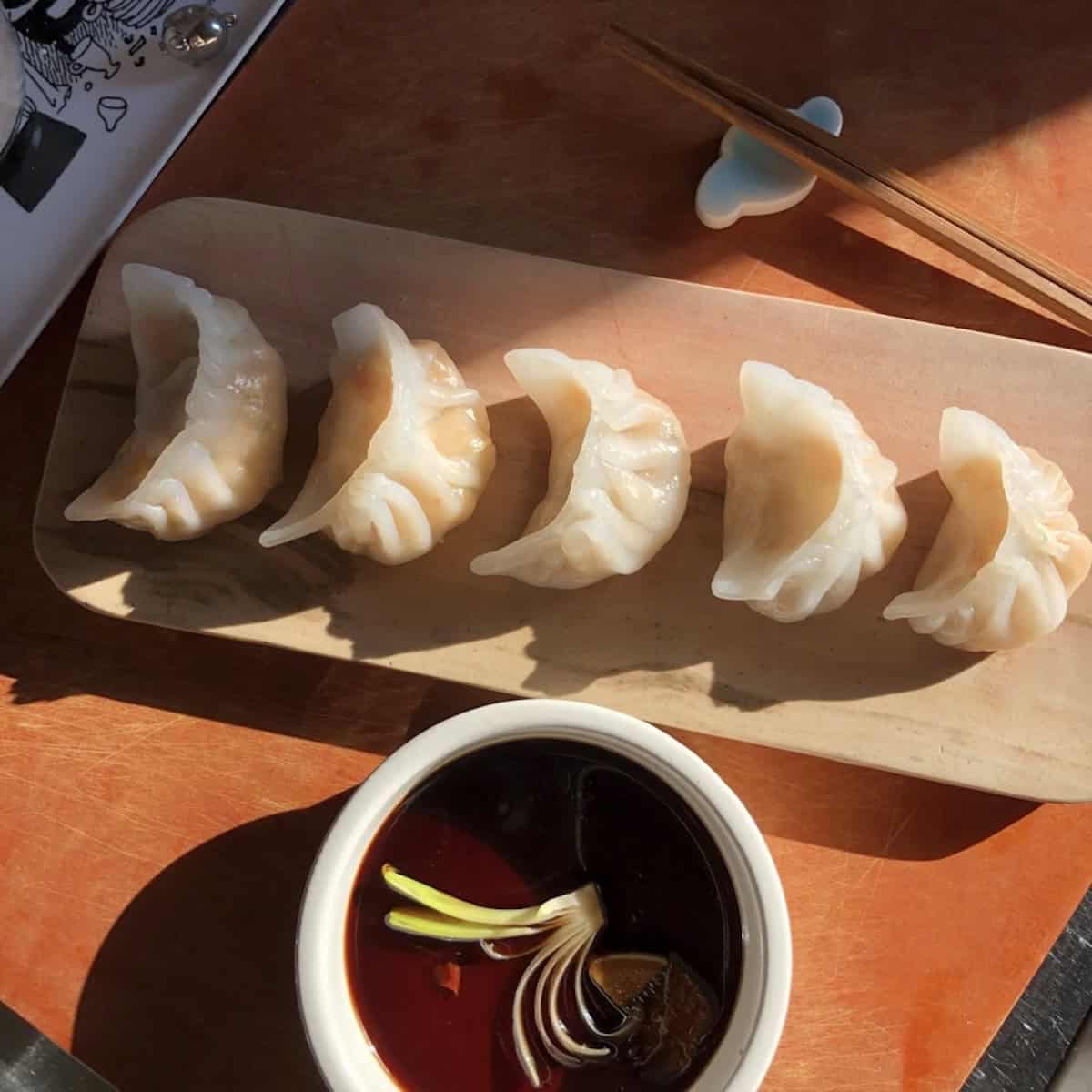 Shrimp dumplings har gow arranged on a tray with dipping sauce garnished with a scallion flower, a classic dim sum recipe.