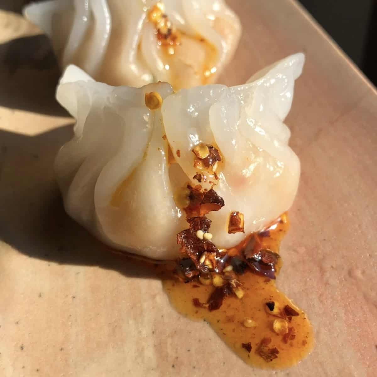 Har gow crystal shrimp dumplings on a pink marble serving platter drizzled with homemade sichuan chili crisp.
