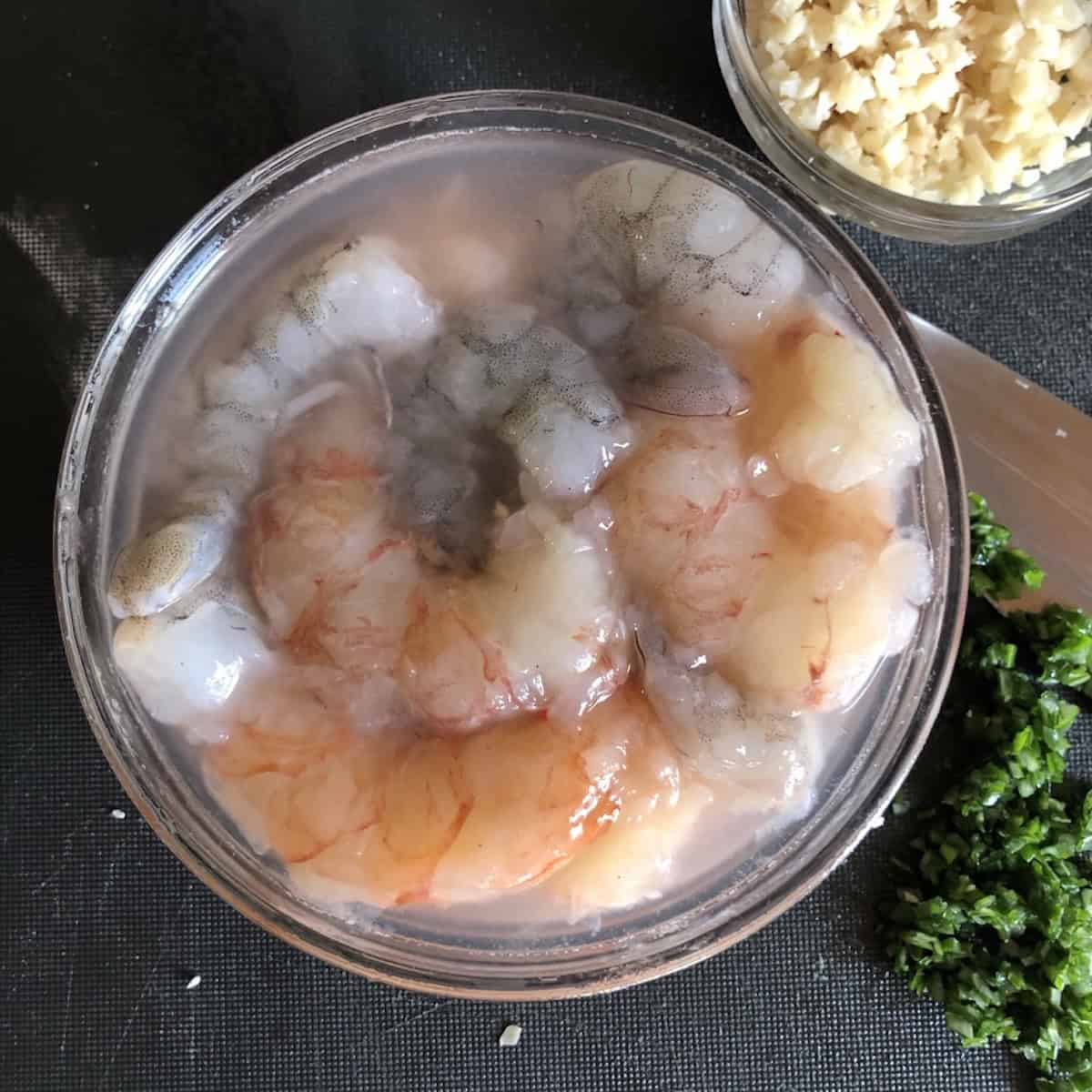 Cleaned and deveined shrimp soaking in a bowl of water and baking soda to improve texture for shrimp dumpling filling.