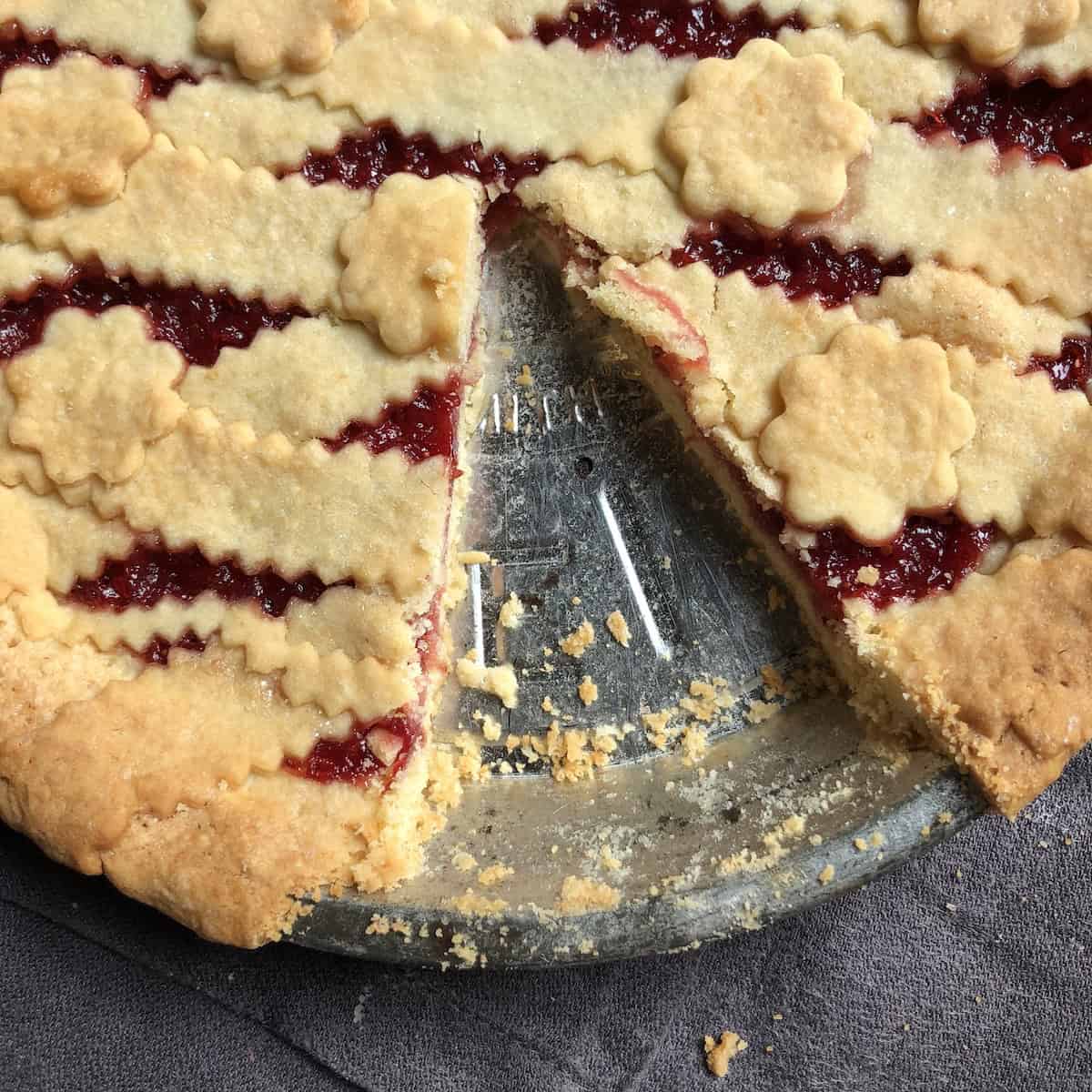Closeup photo of a lattice-topped strawberry jam tart with one piece removed.