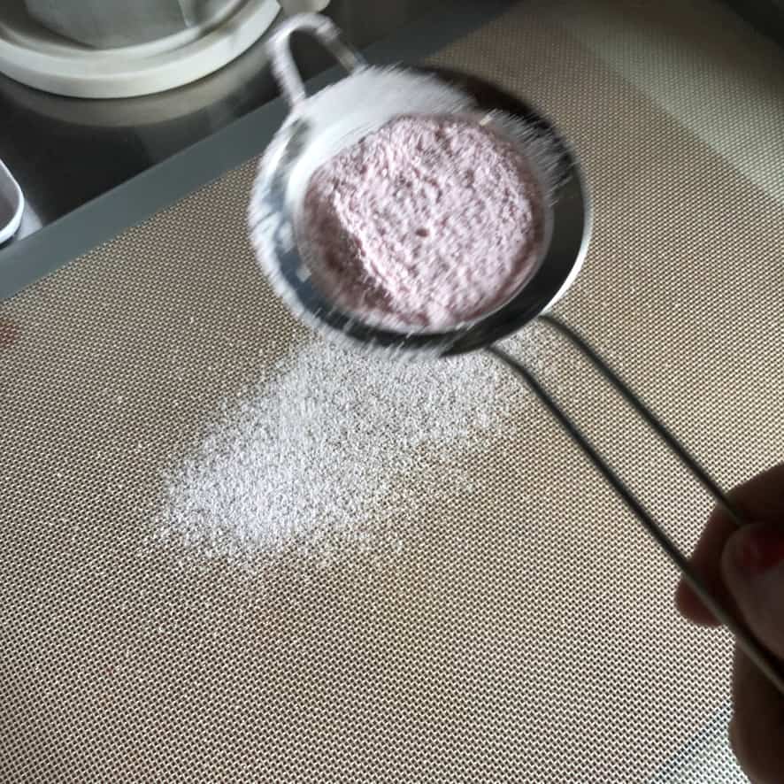 placing sugar, coloring, and cornstarch mixture into a small strainer to dust the work surface