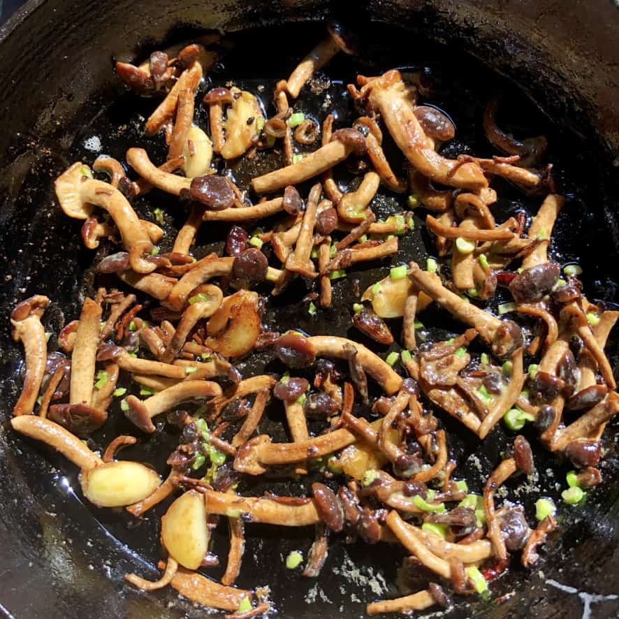 a cast iron skillet full of beautiful golden brown and perfectly seared pioppini black poplar mushrooms with sliced scallions added