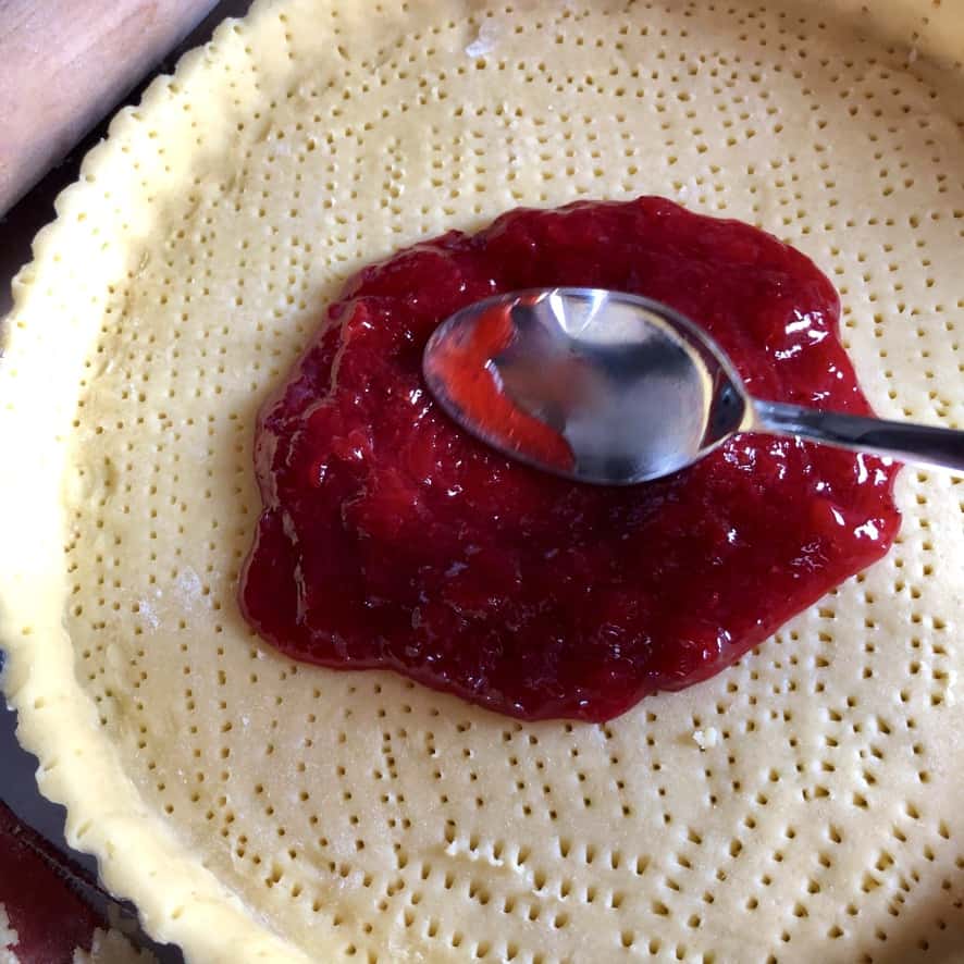 spreading strawberry jam layer in pasta frolla crust