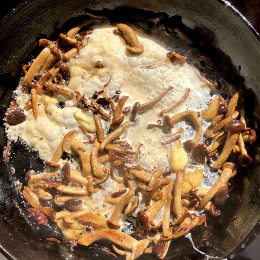 a cast iron skillet full of golden brown sautéed pioppini black poplar mushrooms with a pat of butter and heavy cream just added and boiling up