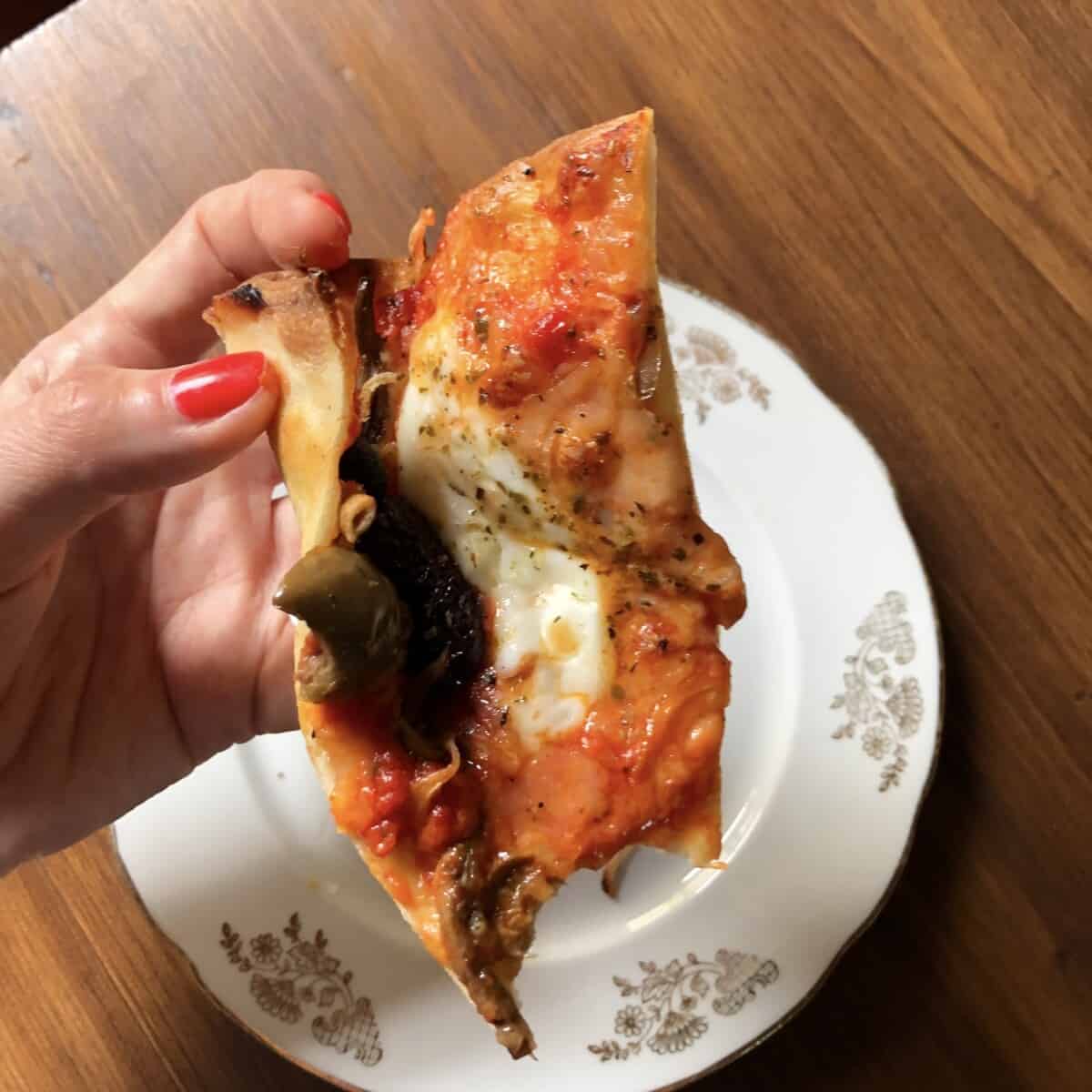 my hand holding a piece of crispy, yet bendable pizza slice with a bite taken out.