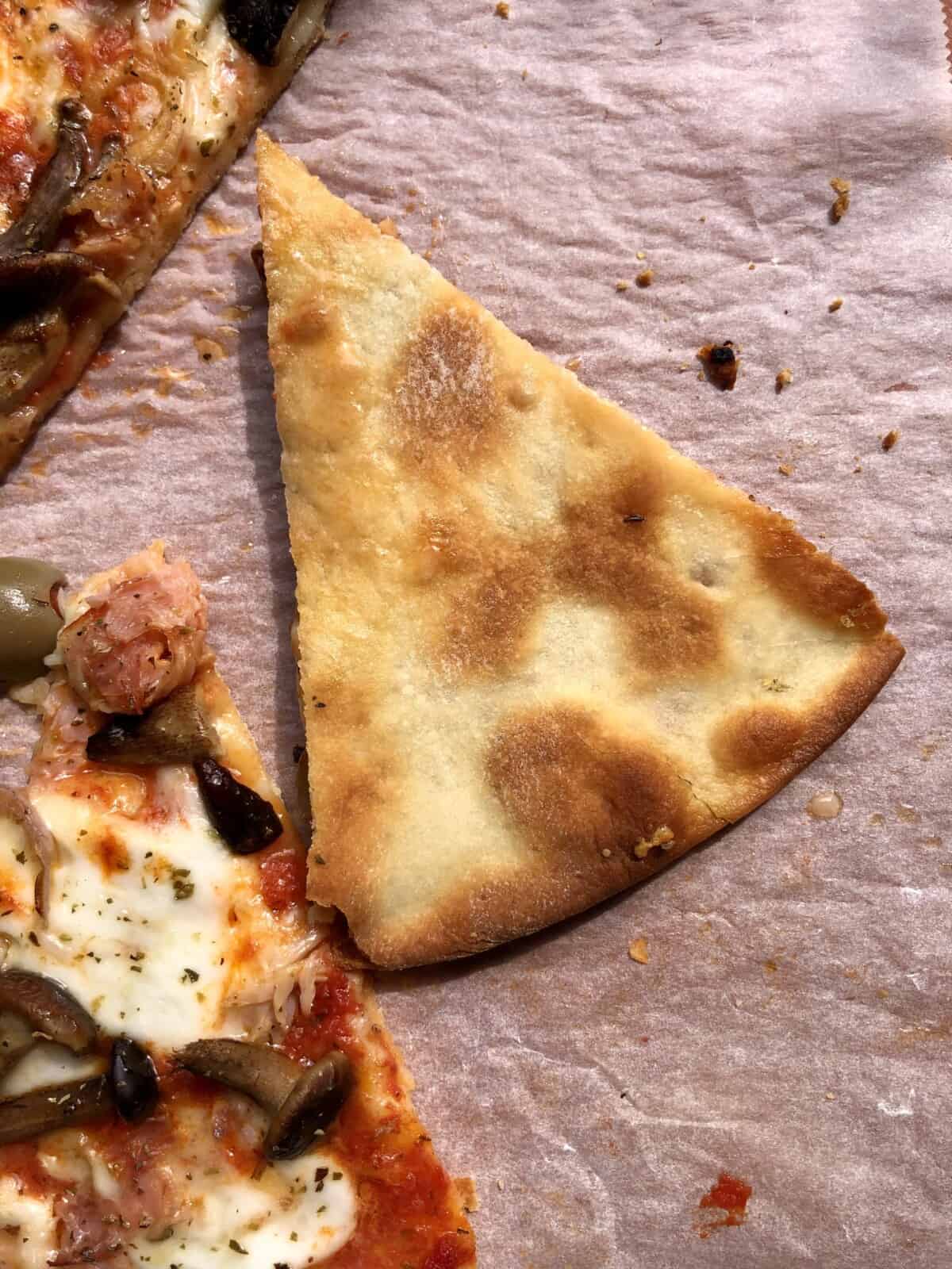 A piece of perfectly baked golden brown crispy thin crust 00 flour pizza turned upside down to reveal the bottom crust and it's beautiful color