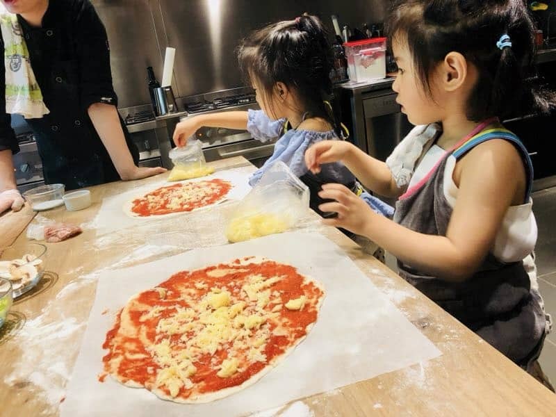 My kids Pizza Making Class in Chengdu, China with 2 super cute and sweet little girls adding cheese to their rolled out pizza dough.