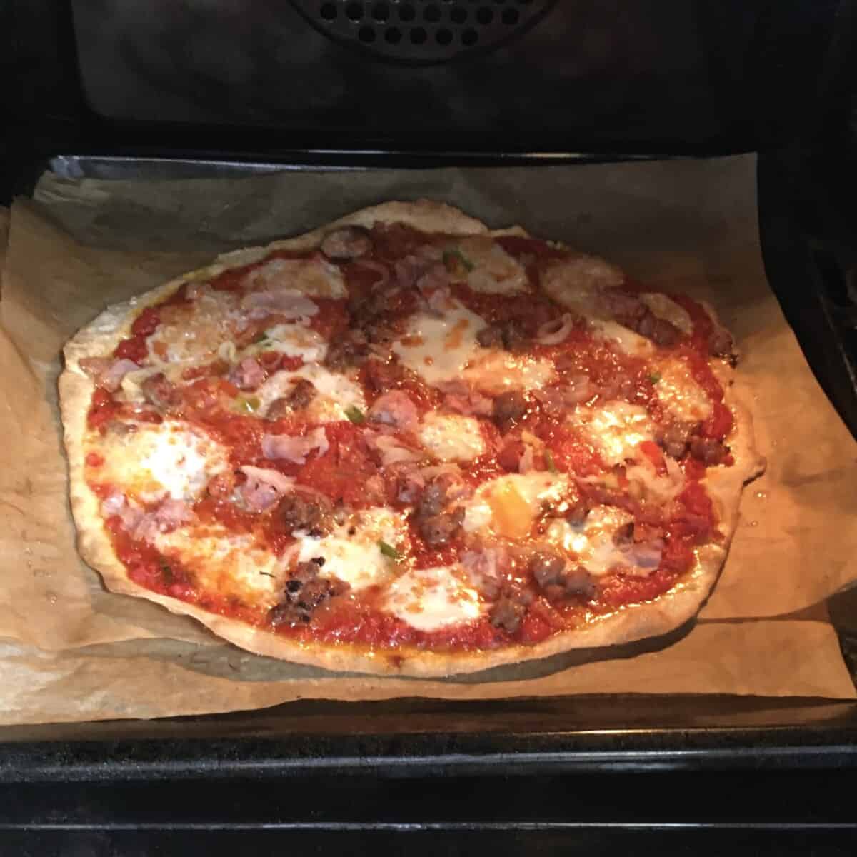 A cracker thin pizza in the oven on 2 pieces of parchment paper in the oven grill pan in the hottest part of the oven (oven floor in this case)