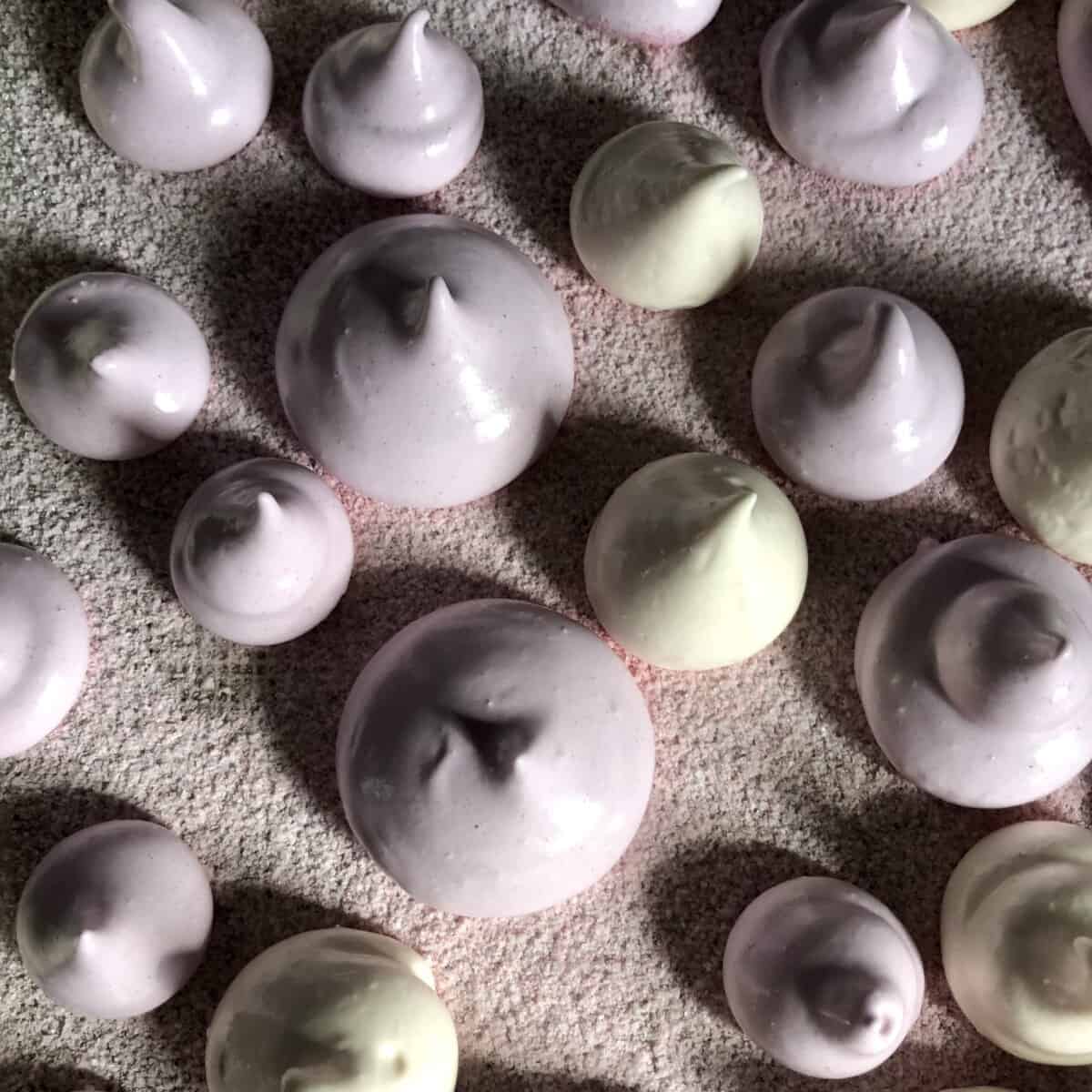 smooth and shiny lavender and white drop-shaped piped marshmallows on a dusted baking tray