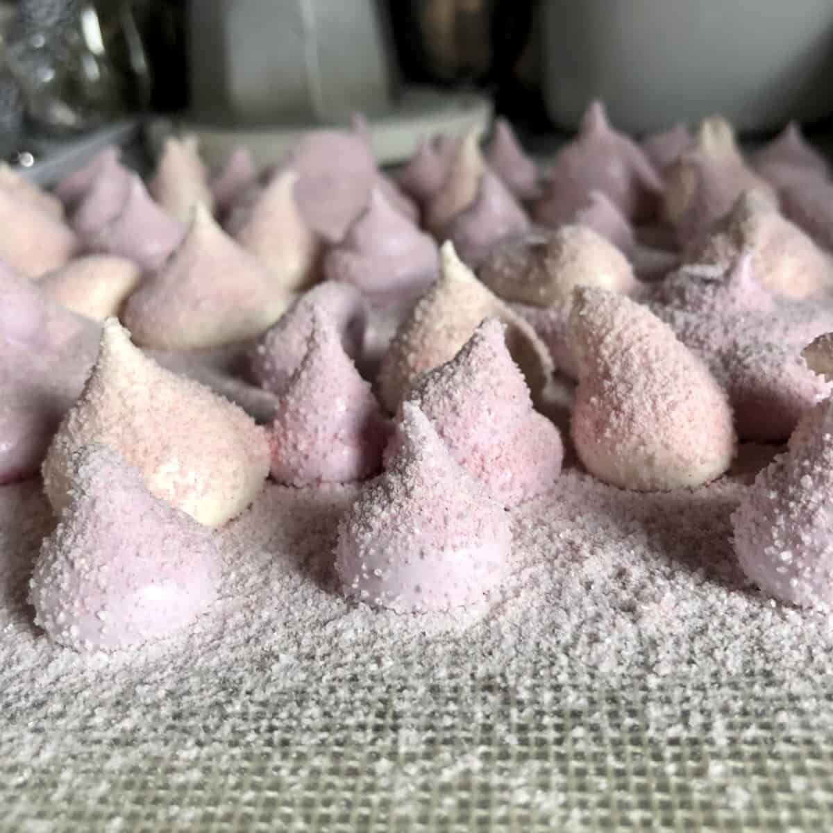 sparkly lavender and white drop-shaped piped marshmallows on a dusted baking tray that have been dusted with coarse sanding sugar and a powdered sugar and cornstarch mixture.