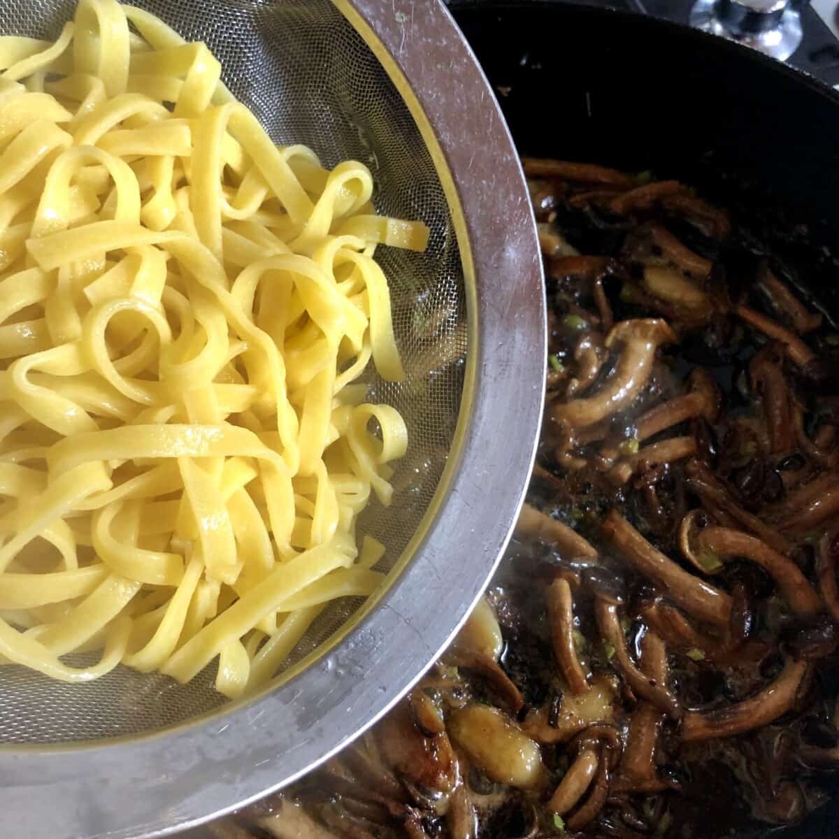 just cooked fettuccine noodles being added to the mushroom sauce