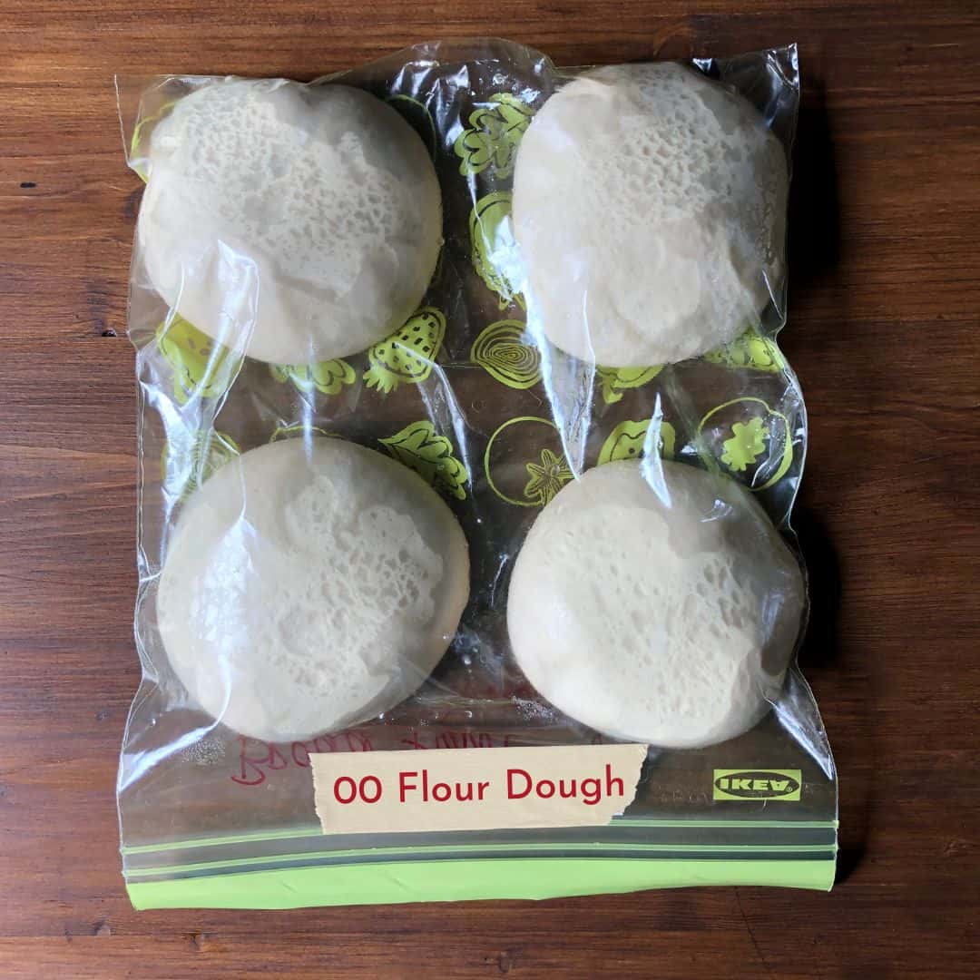 Four homemade 00 flour pizza dough balls in a lightly oiled large zipper bag with all the air squeezed out and the dough balls not touching each other.