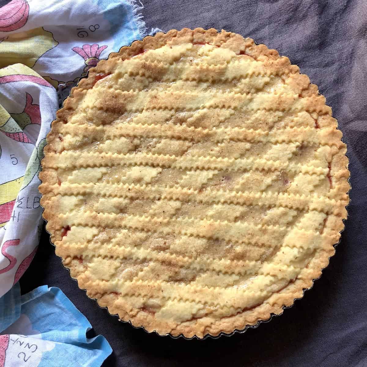 A strawberry cheesecake crostata with lattice-crust on a linen table cloth.