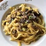 A pasta bowl filled with lightly creamy mushroom pasta sprinkled with grated Grana Padano and chives.
