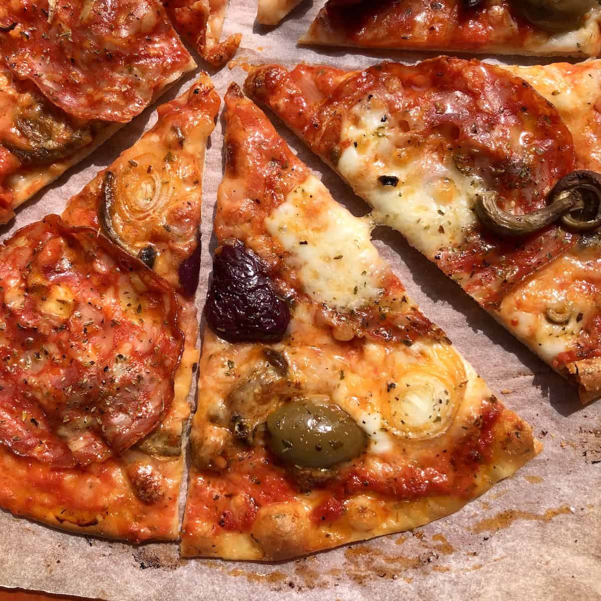 A sliced super crispy thin-crust pizza made using italian 00 flour and topped with spicy ventricina (similar to pepperoni), large cured black and green olives with buffalo mozzarella and whole milk mozzarella. 

