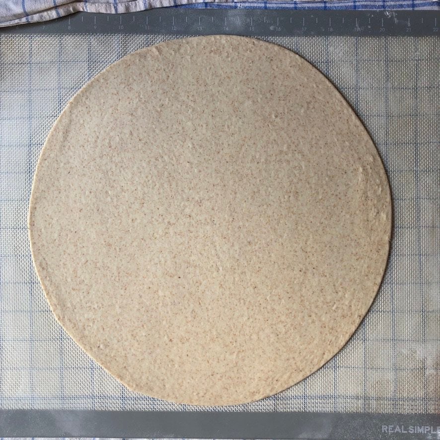 Super thin rolled out pizza dough on a non-stick mat.