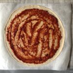 Homemade Pizza sauce spread out evenly across the pizza dough leaving a 1/2 inch border around the edges