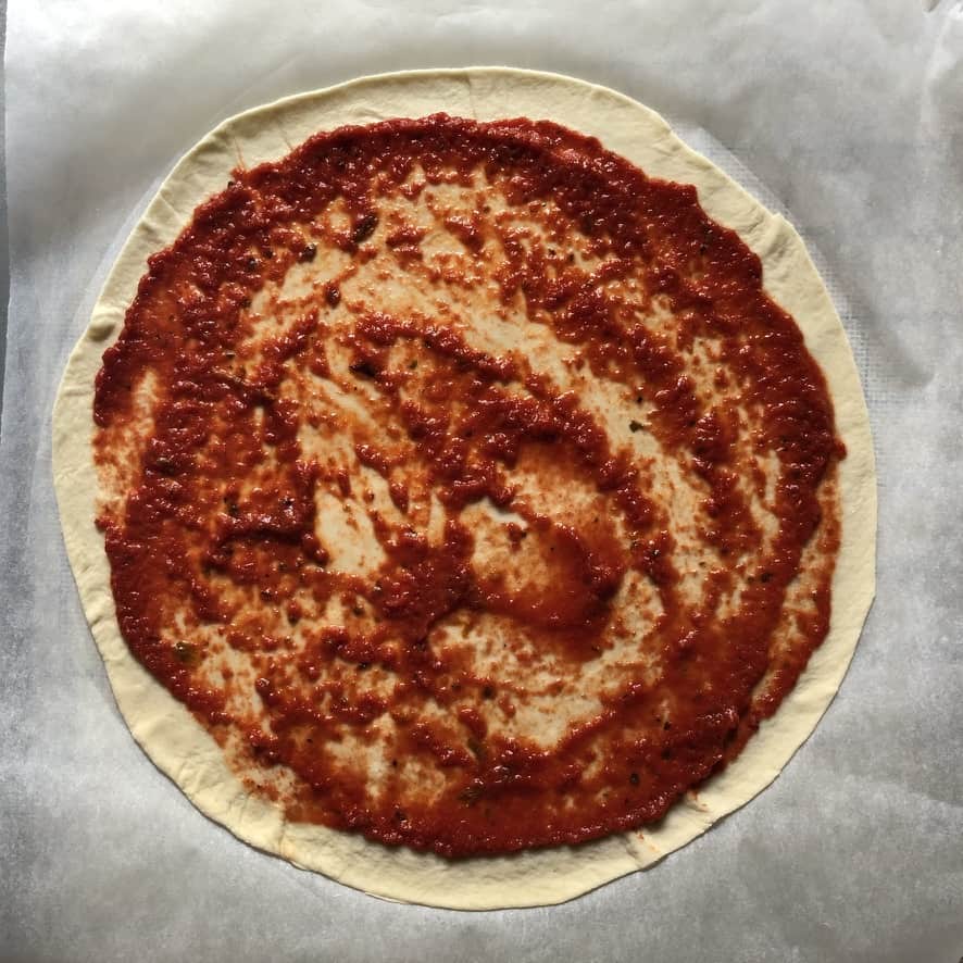 Homemade Pizza sauce spread out evenly across the thin-crust pizza dough leaving a 1/2 inch border around the edges