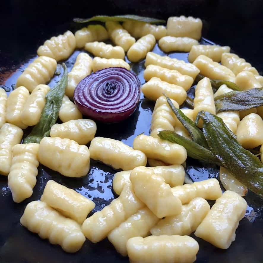 plump, featherlight delicious homemade gnocchi della casa a mia in a skillet being tossed with olive oil, garlic, crispy sage and for a little extra flavor 1/2 a red onion caramalized).