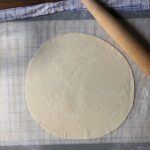 Super thin rolled out pizza dough on a non-stick mat.