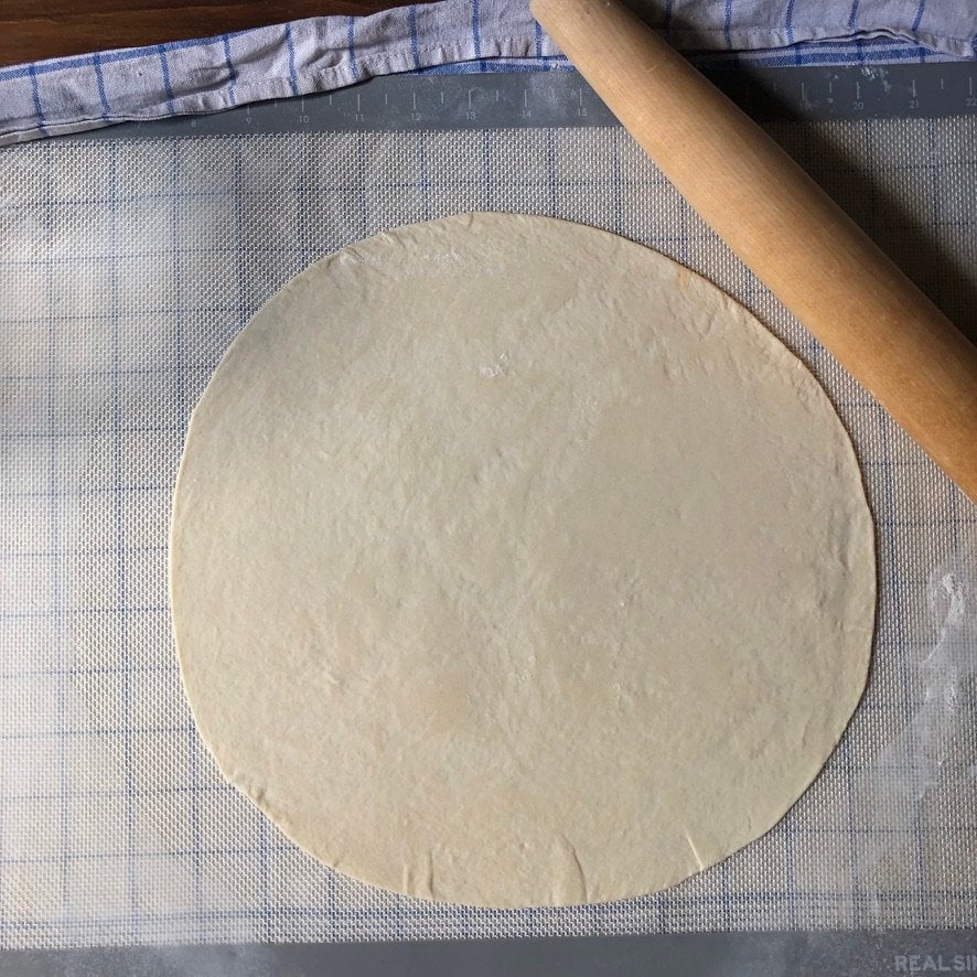 Super thin rolled out pizza dough on a non-stick mat.