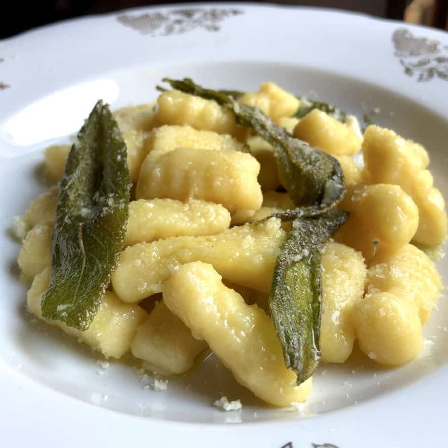 A pasta bowl filled with easy potato gnocchi with fried sage and olive oil with grated Grana Padano cheese.