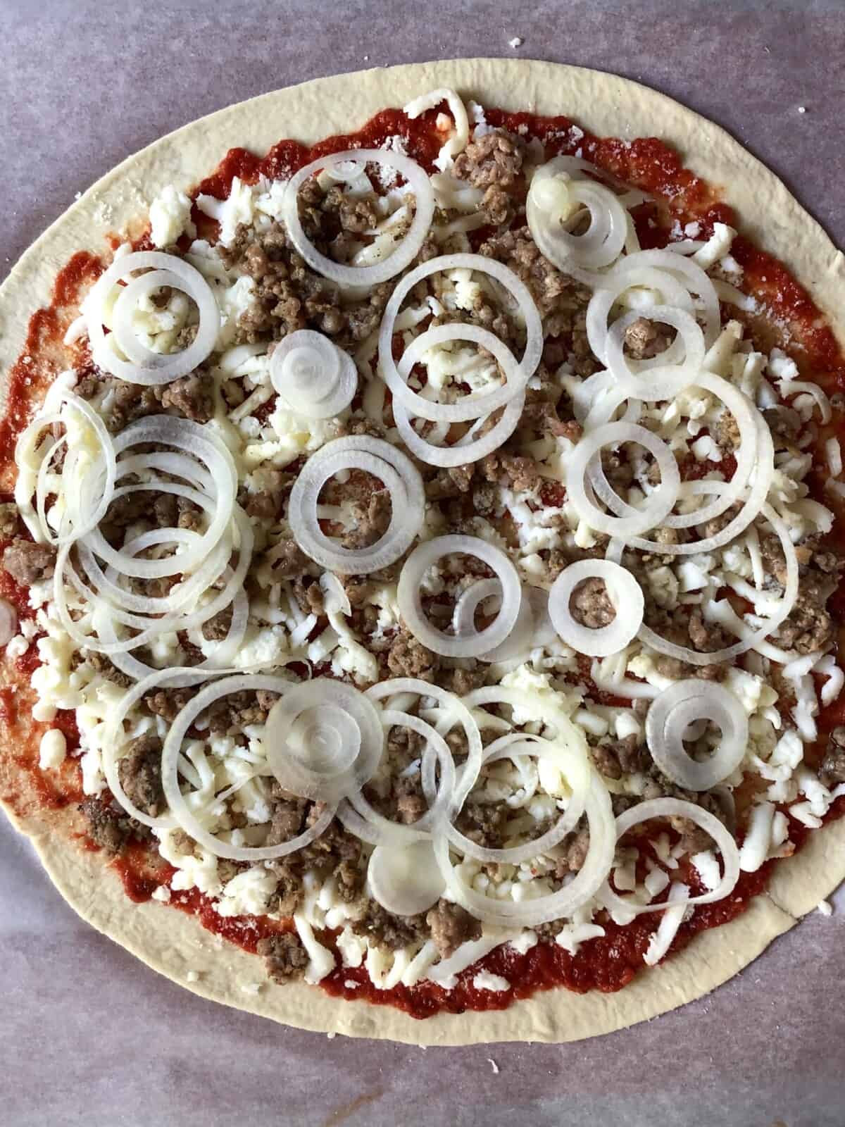 Closeup of fully assembled unbaked sausage and onion pizza