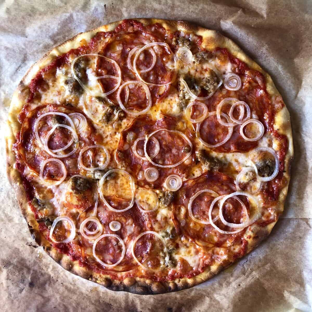 Delicious crispy homemade thin crust pizza with homemade sausage pizza topping, spicy salami, and onions.